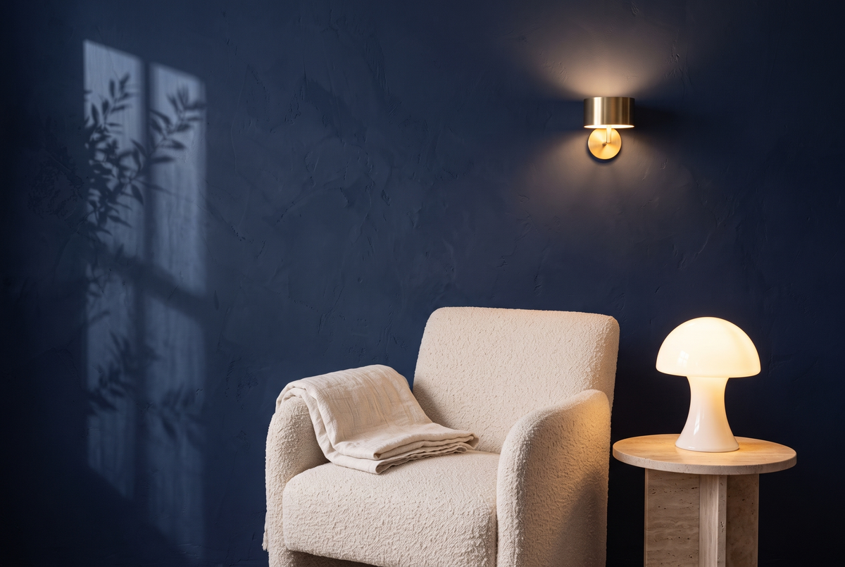 Kabellose Akku-Tischlampe aus Opalglas und kabellose Wandleuchte ohne Kabel neben einem Bouclé-Sessel vor navyblauer Wand
