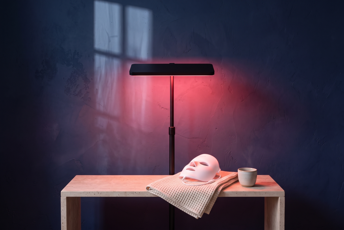 Rotlichttherapie-Panel auf Standfuß mit 660 nm Rotlicht und LED-Gesichtsmaske auf einer Travertin-Bank zuhause
